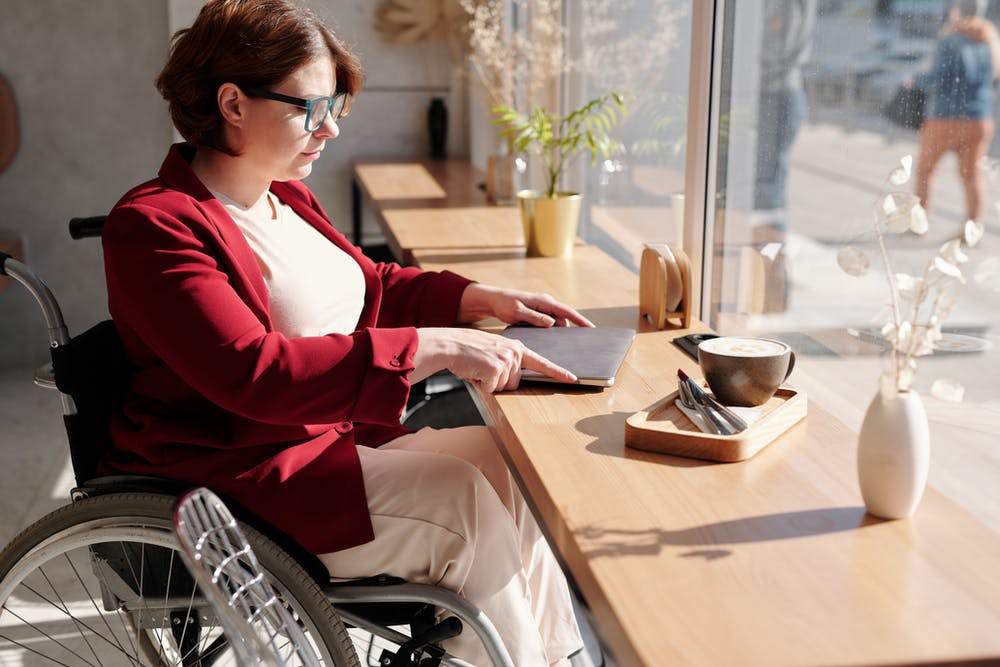 Imagen en la que aparece una mujer en silla de ruedas apoyando sobre una mesa su ordenador portátil