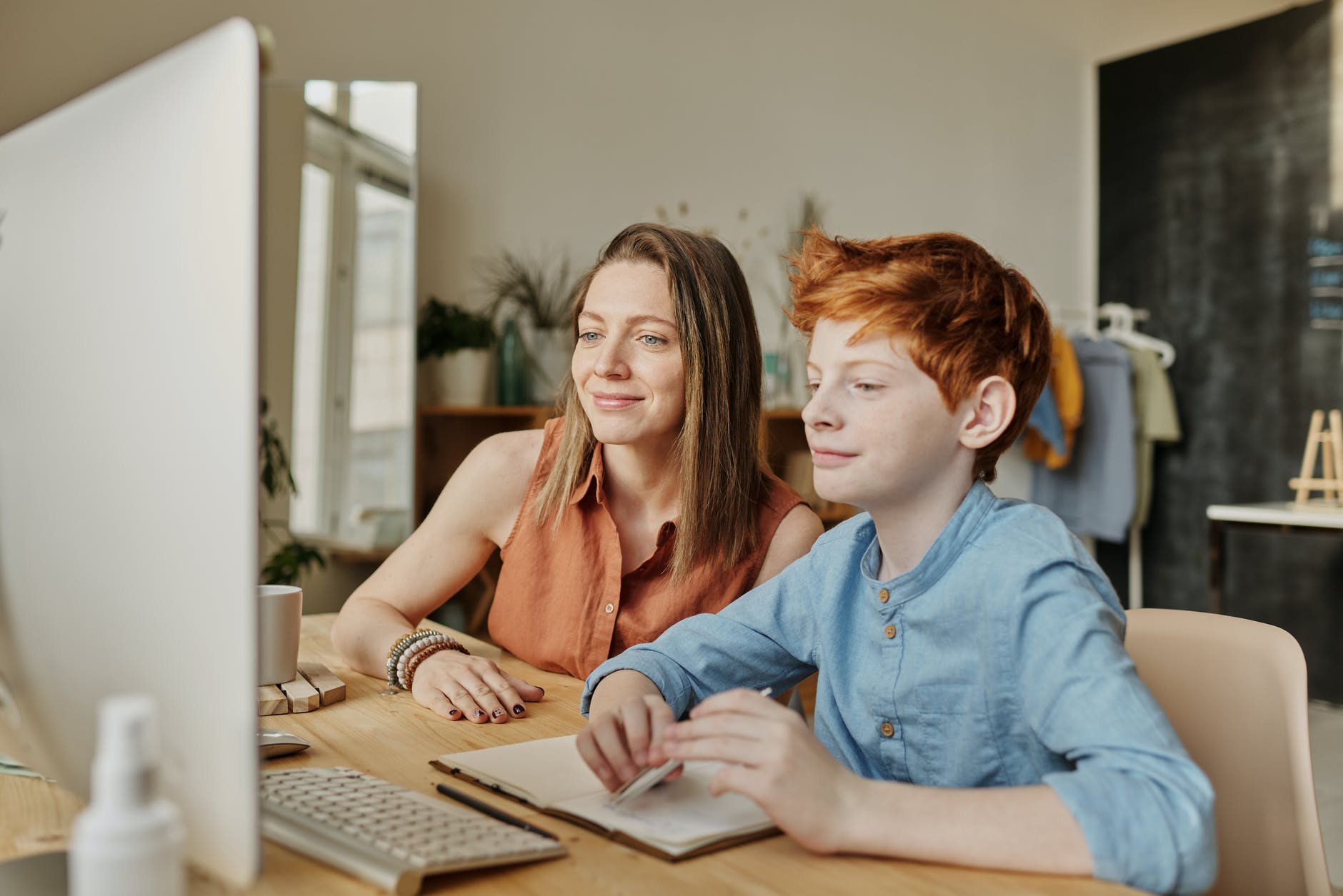 Imagen en la que aparecen una mujer y un niño de alrededor de los 12 años sentados frente a una pantalla de ordenador, mirándo la misma con atención