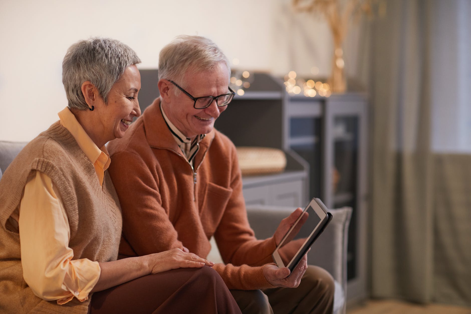 En la imagen aparecen dos personas, mayores de 60 años, sonriendo y mirando con atención una tablet